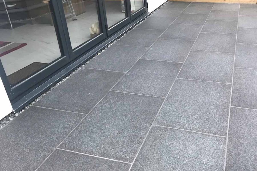 Close-up of basalt porcelain patio pointed with white grout situated in front of bi-fold doors leading to the living room area.