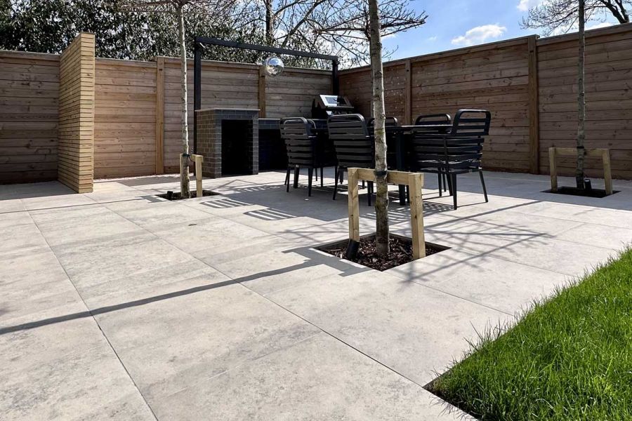 Jura Grey Porcelain paved courtyard on a winters day surrounded by timber screening and featuring pleached trees and a dining set.