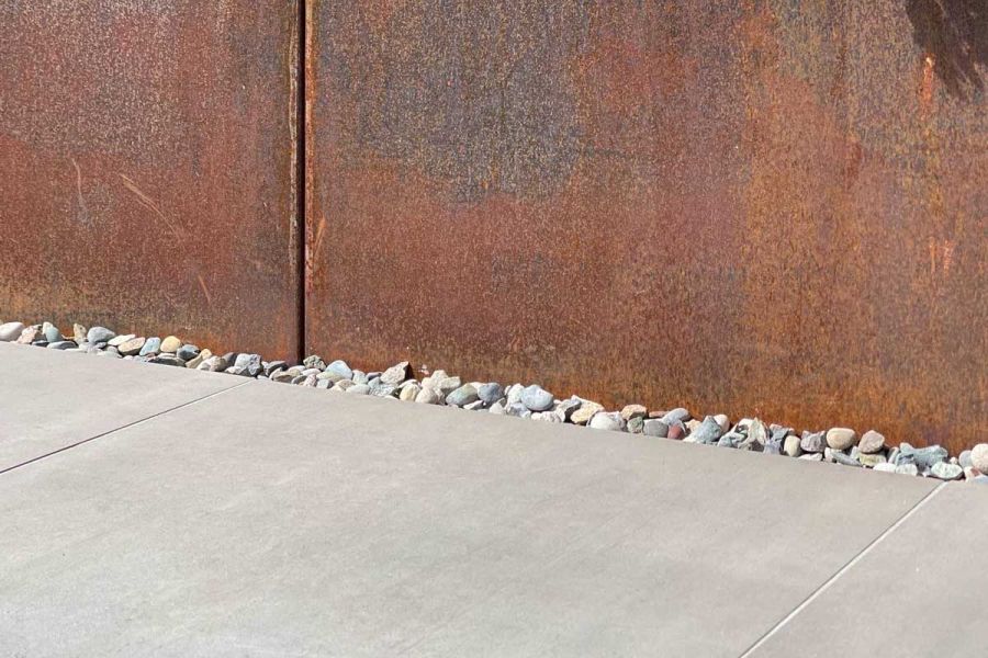 Close up photo of Polished Concrete porcelain paving slabs sat up against Corten Steel garden planters separated by a narrow pebble strip.