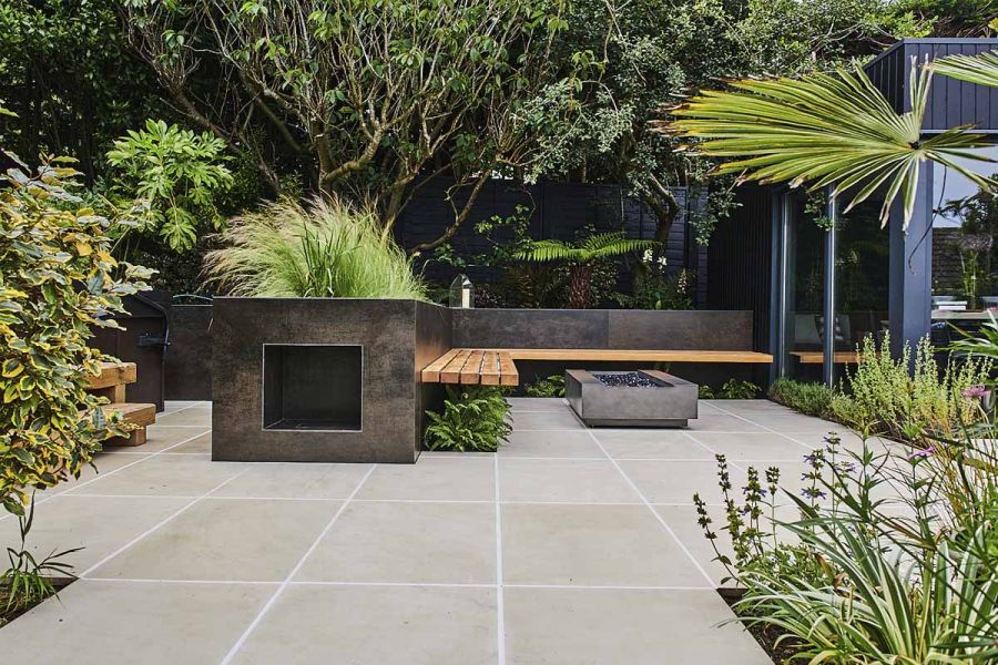 Architectural planting surrounds Beige Sawn Sandstone paving laid stack bond, with firepit, wooden benches and raised beds.