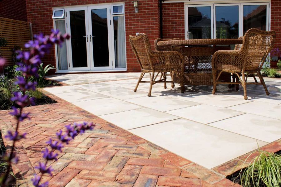 Dining set on cream patio with Cotswold clay brick edging and path outside 2 sets of french doors. Built by Essex Garden Designs.