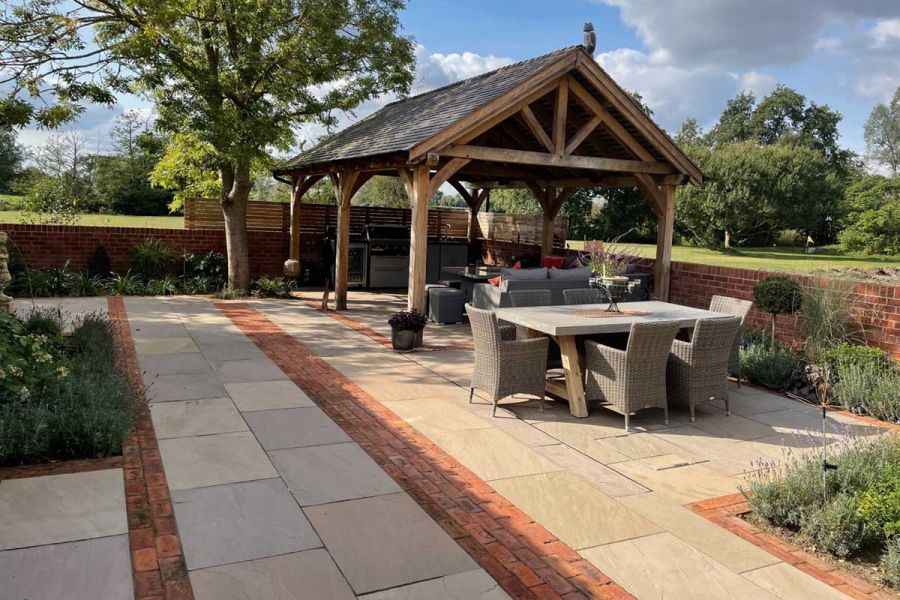 Natural stone paved area with Romsey Antique Clay pavers detailing. Dining set and roofed pergola. Design by Roger Gladwell.