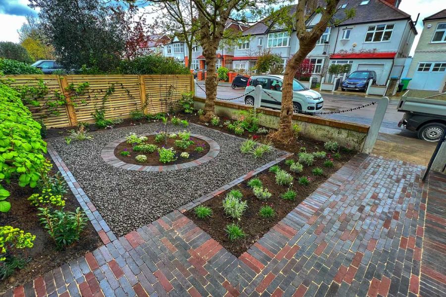 Round planted bed sits in centre of gravel square edged with grey and red mixed Moderna and Bergamo clay pavers in front garden.