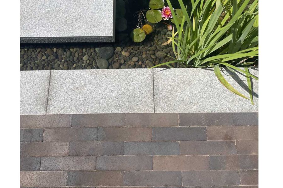 Chelsea clay pavers with sanded joints laid with granite paving edge above pond with iris plants. Built by Big Fish Landscapes.