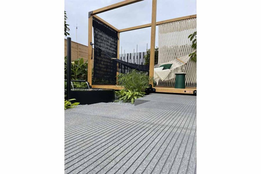 Black granite paving with bespoke grooves in surface leads to large wooden frame containing black and white hammock.