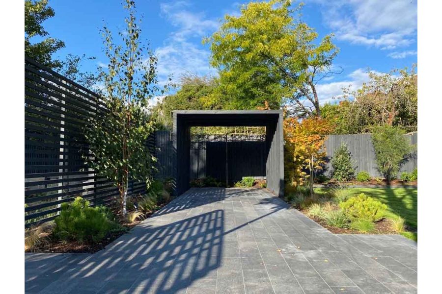 Between fence and lawn with planted beds, Black granite plank paving runs lengthways to garden shelter. Built by Natural Spaces.