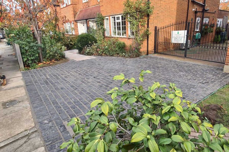 Paving of Natural Black Granite setts narrows to meet stone slab path across front garden of period suburban house.