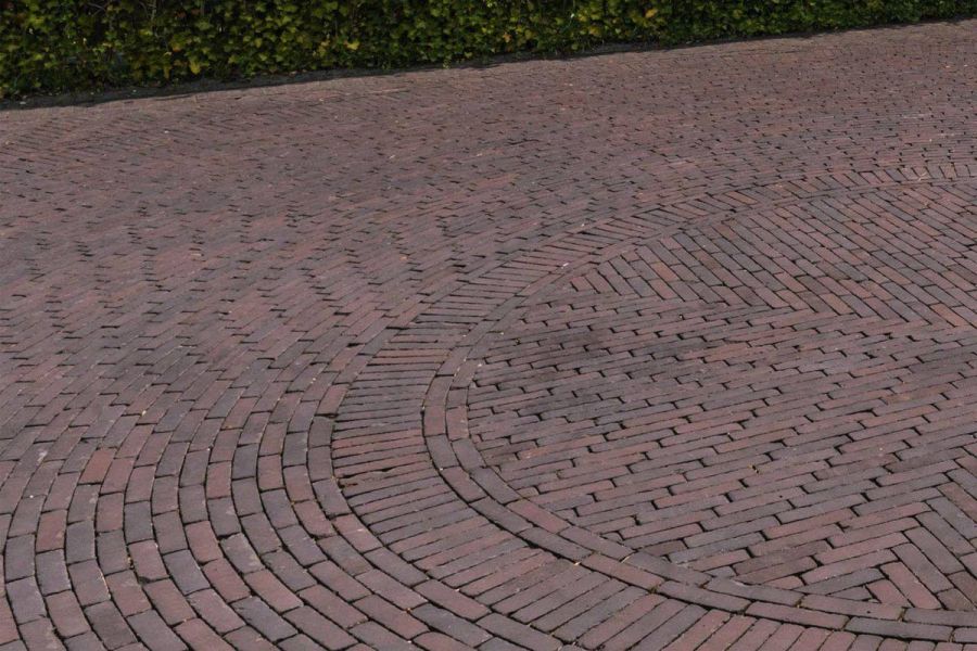 Paved area of Bolzano brick paving laid in different directions to create a circular pattern next to hedge.