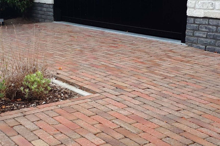 Low view of Seville clay pavers laid running bond, edged by grey and white-painted walls and black garage door. 
