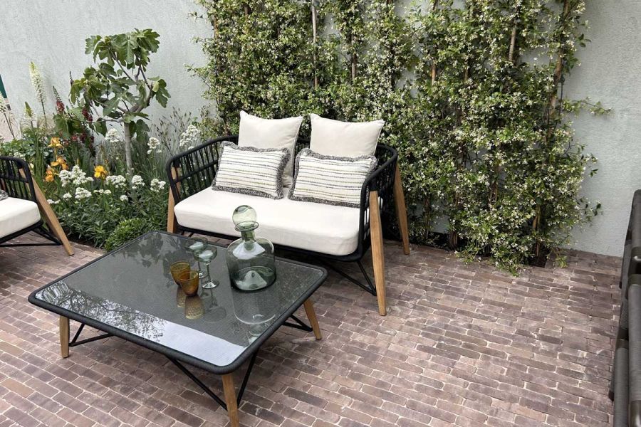 Narrow bed planted with tall shrubs behind white cushioned sofa with coffee table on Verona light red clay brick paving.