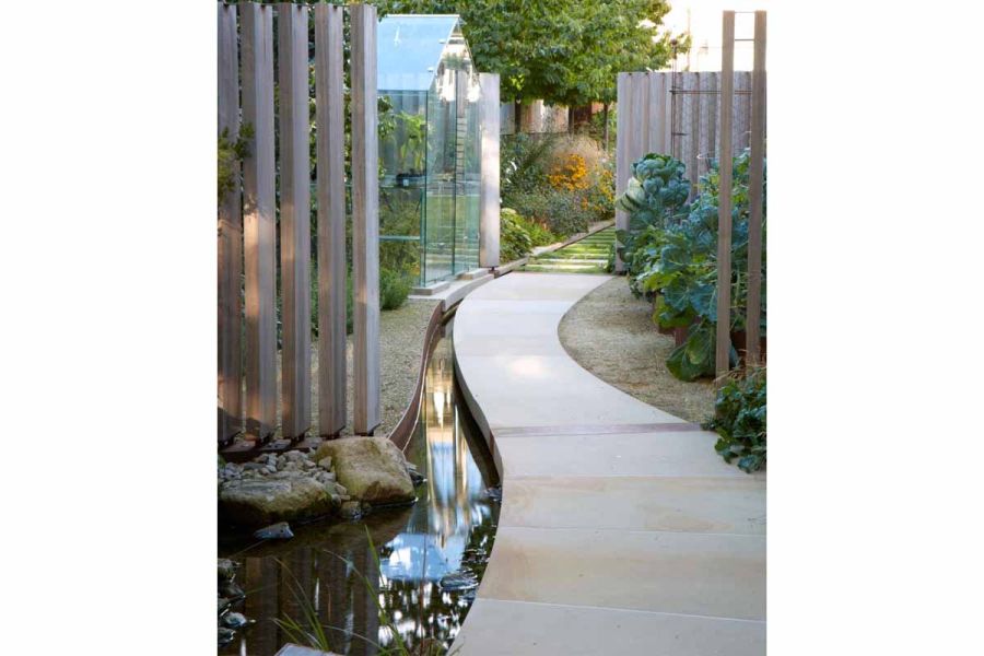 Sinuous Britannia Buff sawn York stone path of bespoke slabs leads along rill past greenhouse to lawn with stepping stones.