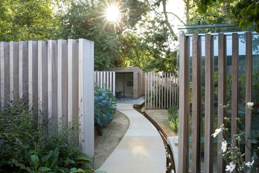 Curved path of bespoke Britannia Buff sawn Yorkstone paving runs towards garden room between upright wooden plank features. 