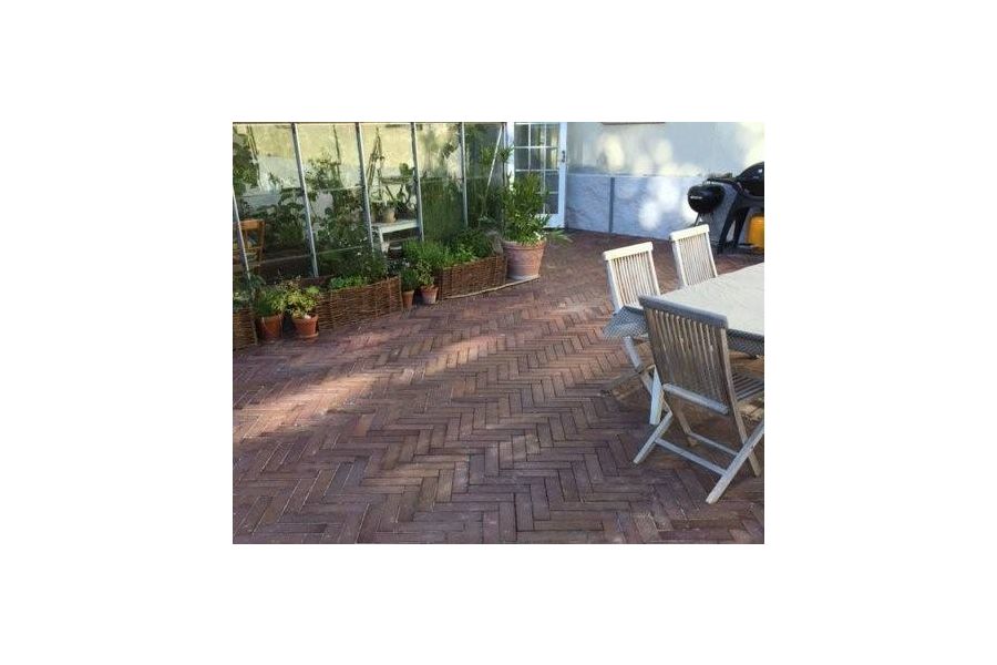 Dappled area, with wooden dining set and greenhouse against white wall, paved with Bromley clay paving bricks laid herringbone.