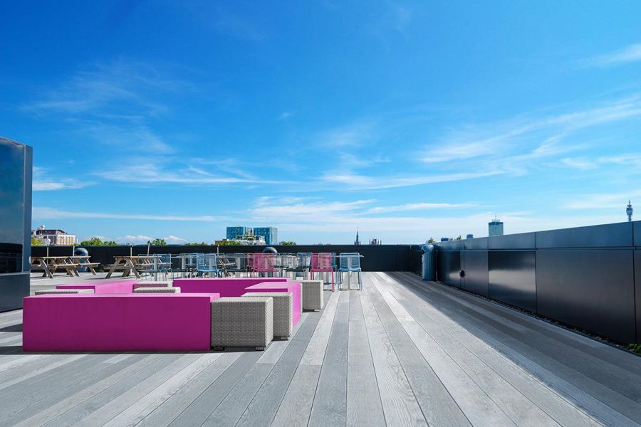 Large roof terrace laid with long planks of grey Enhanced Grain Decking. Various seating options are spread across the area.