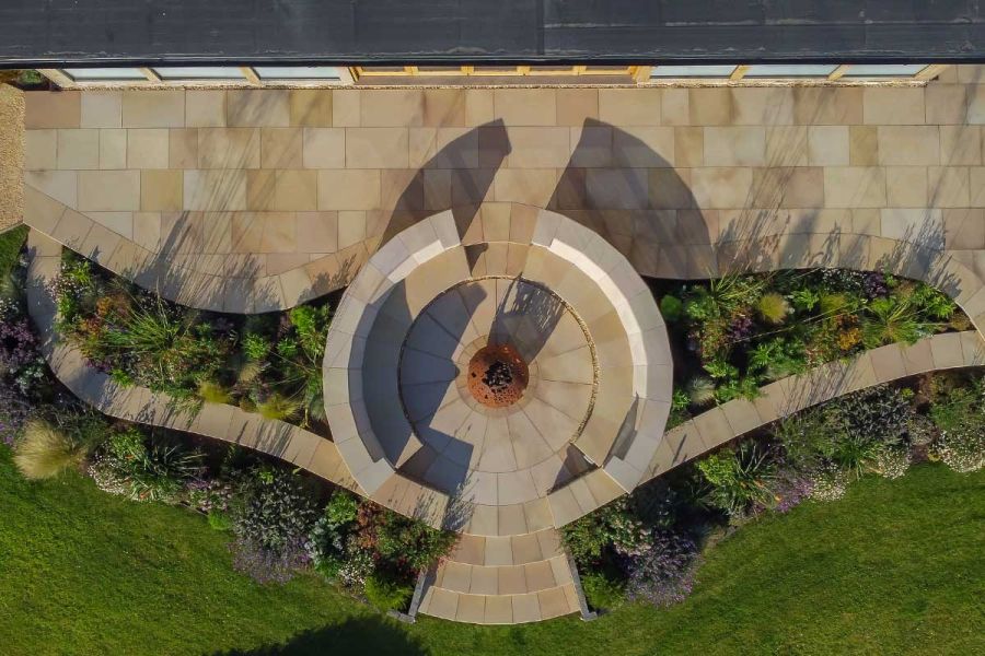 Aerial view of patio and circular sunken seating area with central metal fire globe, paved with radially cut buff sawn sandstone.