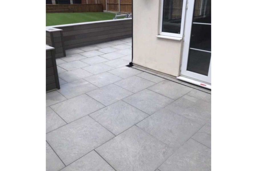 Astor Grey porcelain paving patio with slot drain wraps around corner of white house. Built by C Howell Builders and Landscapers.