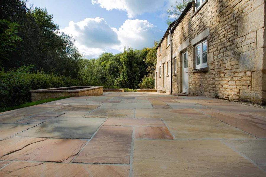 Long patio of Camel Dust Indian sandstone at rear of large rural cottage. 3 deep planting pits in matching stone on edge of paving.
