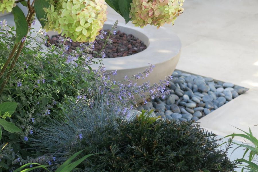 Close-up of planted area located next to a water feature bowl placed on pebbles next to Cement Porcelain garden tiles.