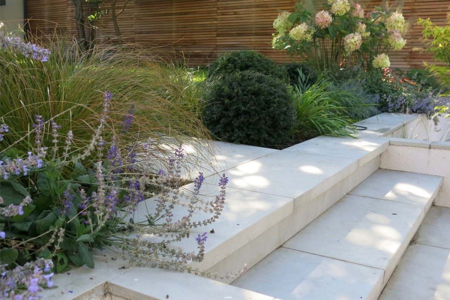 Grey Cement porcelain paving laid with garden steps and coping stones surrounded by an abundant and colourful planting scheme.