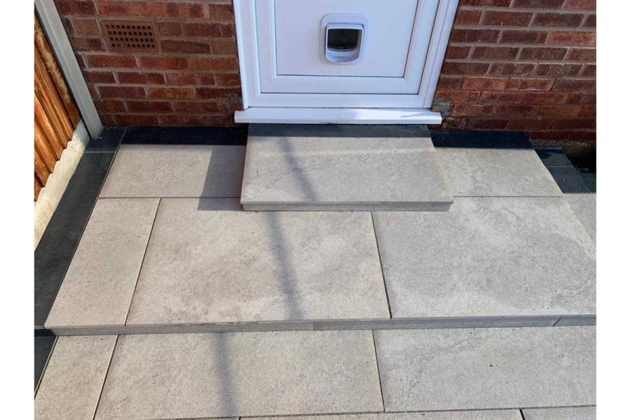 2 shallow steps down from back door to light grey patio edged with Charcoal porcelain planks. Built by C and C Agricultural.
