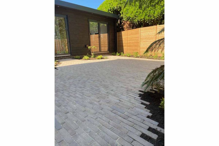 Large area of Charcoal Grey clay pavers laid in running bond pattern, creating staggered edge to flower bed at rear of modern house.