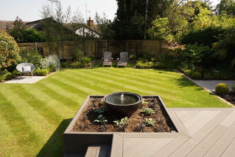 Fenced garden with lawn seen from raised Charcoal composite deck with bowl water feature on planted bed forming corner edge.