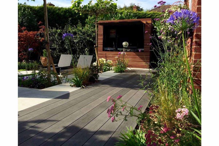 Charcoal Designboard composite decking separates planted border from paved area with 2 loungers edged by hedge and slatted screen.