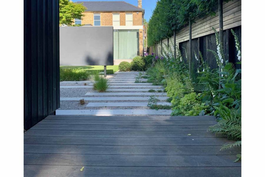 Charcoal DesignBoard leads to plank paving, set in gravel, which runs down edge of fenced garden to house. Design by Tom Howard.