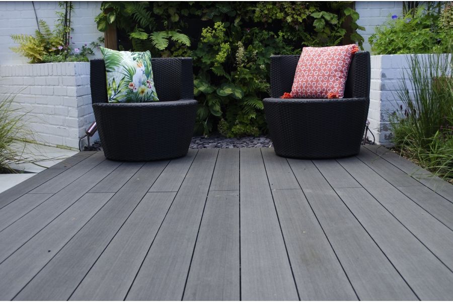2 black chairs sit on Charcoal DesignBoard WPC decking in front of living wall between white raised beds. Design by Botanica.