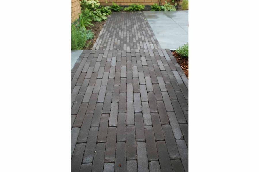 Charcoal Grey clay paving path runs parallel with slatted fence, past potted plant and barbecue stand faced with matching pavers.