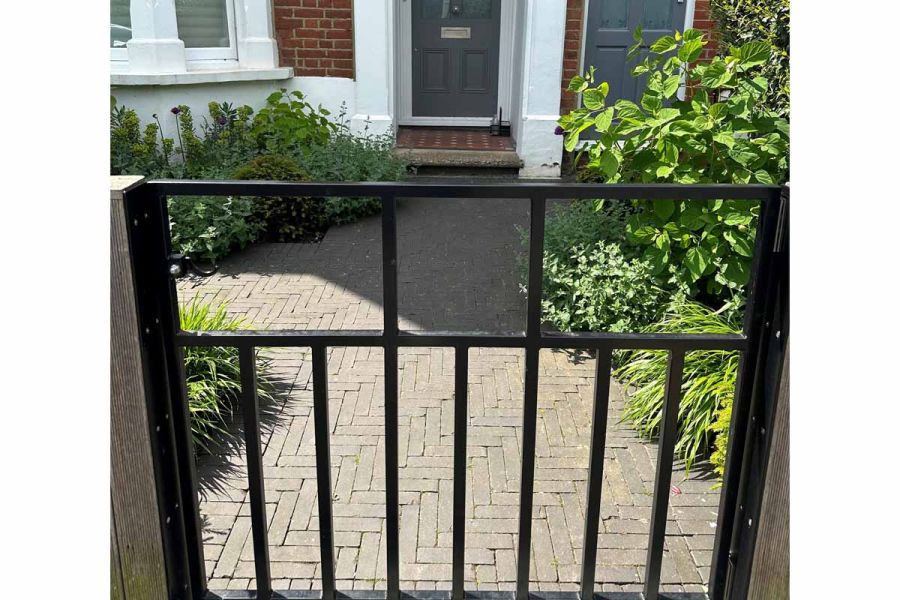 View through front gate shows Charcoal Grey Clay paving leading up to doorstep in herringbone pattern. By Fiona Lamb.