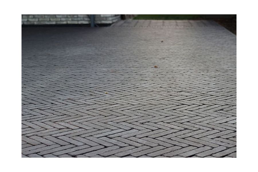 Low shot of charcoal grey clay pavers laid in a herringbone style, sunlight setting in the background.