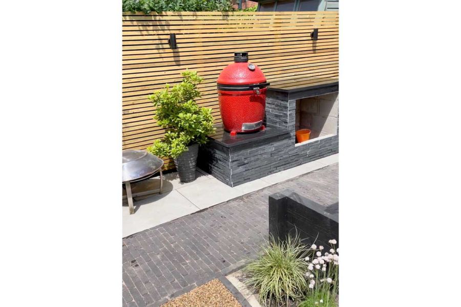 Path of charcoal grey clay pavers runs through and outdoor kitchen, with red bubble BBQ proudly on display beneath grey cladding.