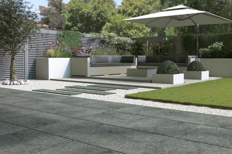 Charcoal porcelain paving and stepping stones leading towards a raised composite decking terrace with seating and large parasol.