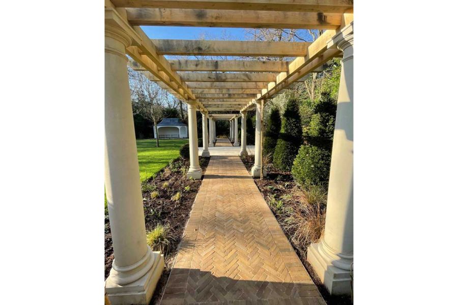 Stone-pillared colonnade stretches into distance towards summer house, over path laid herringbone with Westminster Clay Pavers.