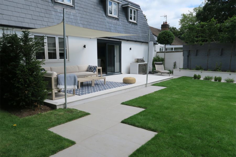Urban Grey Porcelain path with zigzag edges leads to decked area by house, covered by shade sail. By Cherry Mills Garden Design.