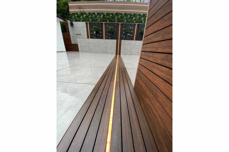 Chestnut Composite Screening Battens laid on the floor in between porcelain paving patio, featuring led strips.