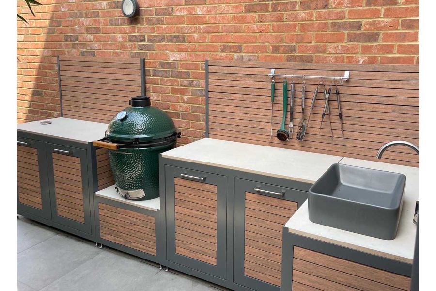 Utensils hang on Chestnut composite batten screen against wall, behind outdoor kitchen units with doors in matching cladding.