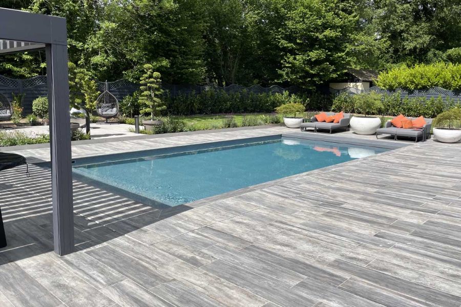 Large pool next to a pergola hosts 2 sunloungers at the end, with Cinder Porcelain Paving used around.