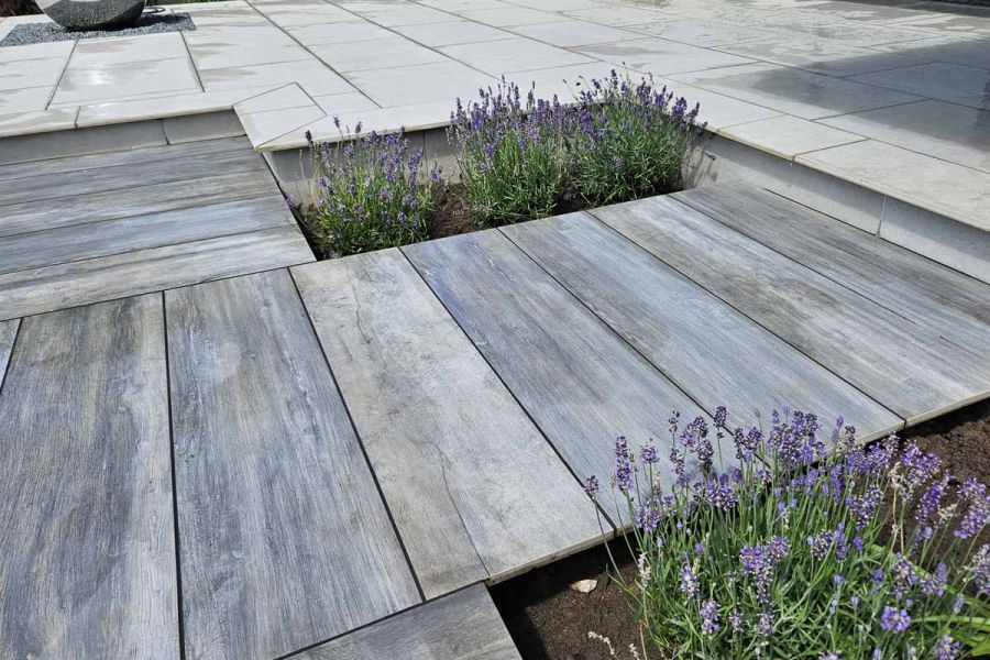 Close up view of Cinder porcelain paving, showing its unique texture and wood like effect with lavender planted either side.