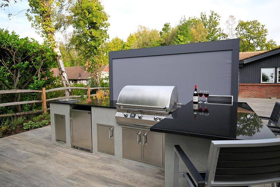 Outdoor barbecue and kitchen area with granite work tops and large outdoor screen sat on top of a Cinder porcelain patio.