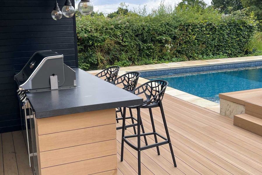 Decking area in Cinnamon DesignBoard composite planks with 3 tall stools at bar next to swimming pool. Built by Mann Contractors.