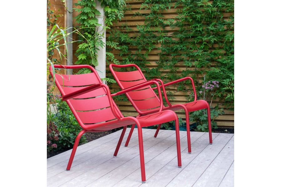 2 red chairs sit in corner of Cinnamon composite decking, slatted fence with climbers in background. Design by A Ryan-Mills.