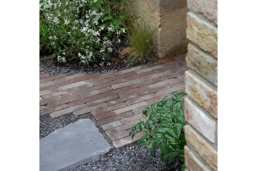 Ragged-edged path of Bergamo Clay Pavers laid in grey gravel with natural stone slab next to Choisya. Built by Big Fish Landscapes.