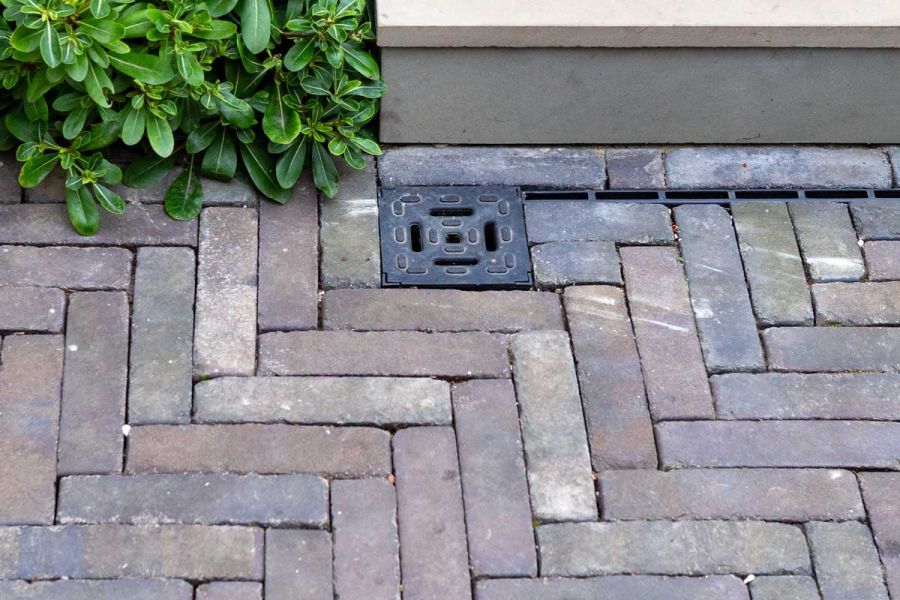 Square metal drain plate set into Ancona grey clay pavers laid herringbone by Acacia Gardens in design by Daniel Shea.