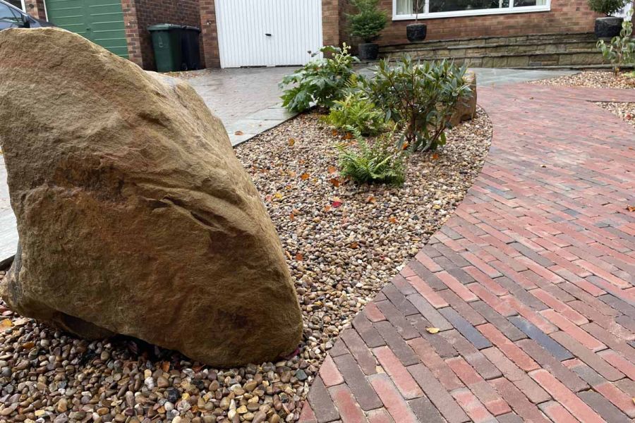 Curved path of Bexhill clay paving, with cut edges, leads to front of house next to boulder and plants set into gravel.