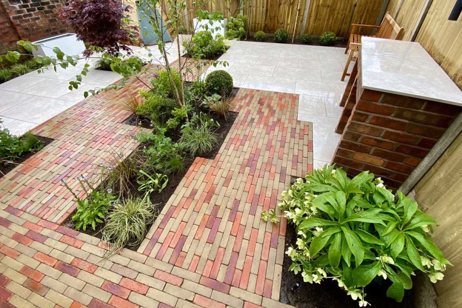 Westminster and Seville Clay Paving with porcelain tiles in fenced garden with planted beds and bench. Built by Bark Brick & Block.
