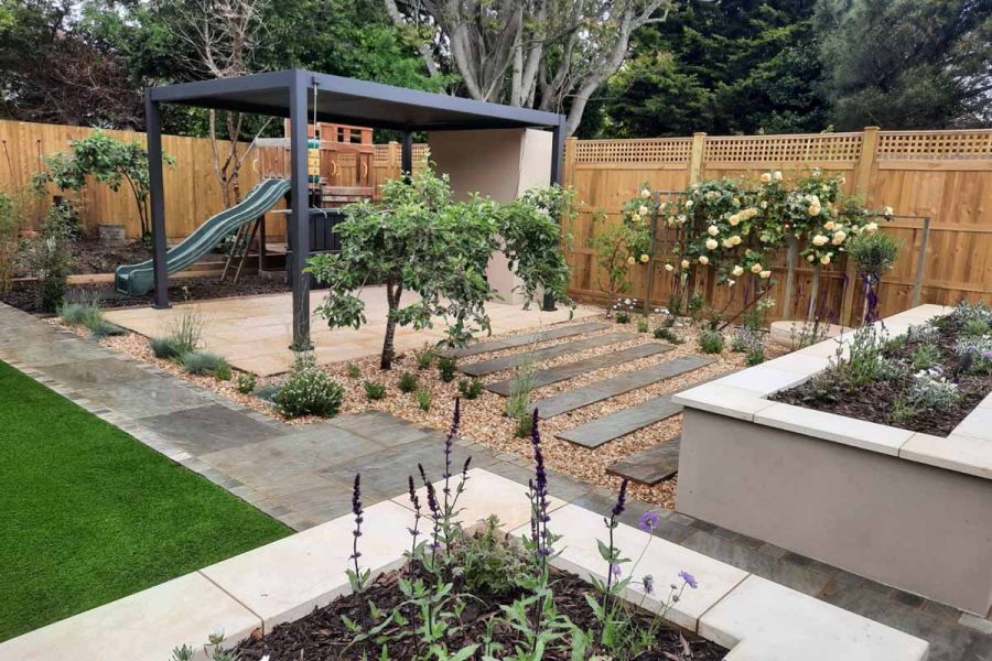 busy family garden, raised planters to the right and play area on the left with kandla grey indian sandstone path running through.