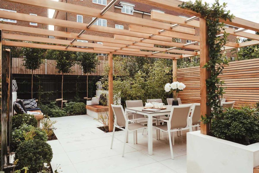 Large pergola covers Comblanchien Porcelain Paving, white outdoor dining set, and slatted fencing. Design by Langdale Landscapes.