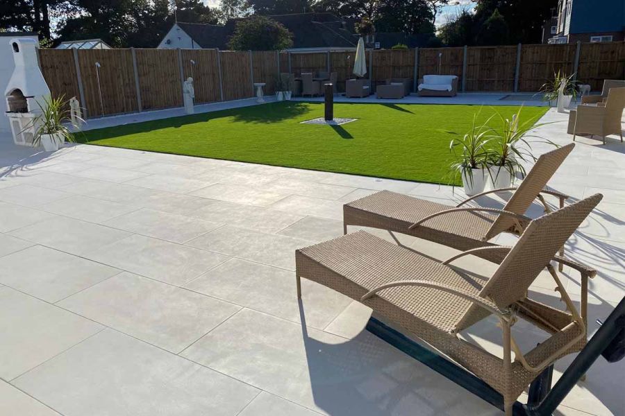 Garden space paved with Comblanchien vitrified tiles, featuring central grass area and rattan sun-loungers to relax on.